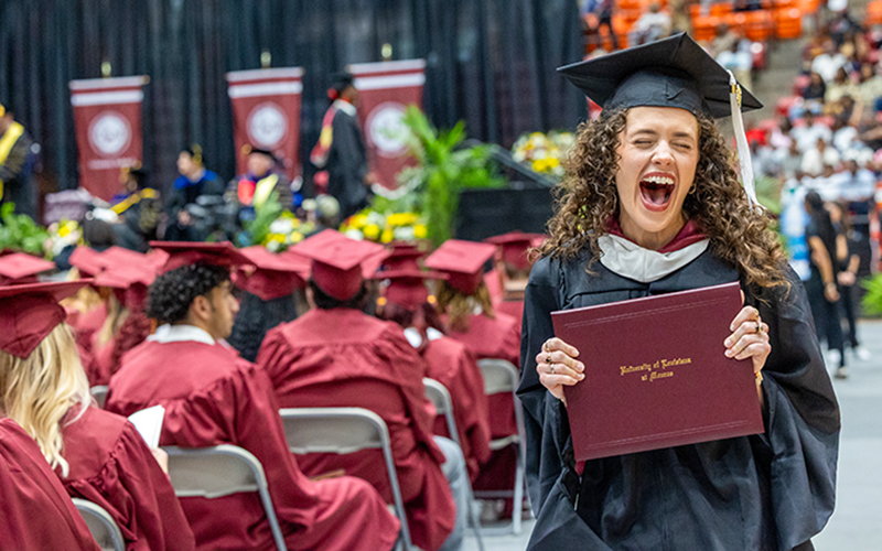 ULM student wearing a graduation cap and gown holds a diploma.