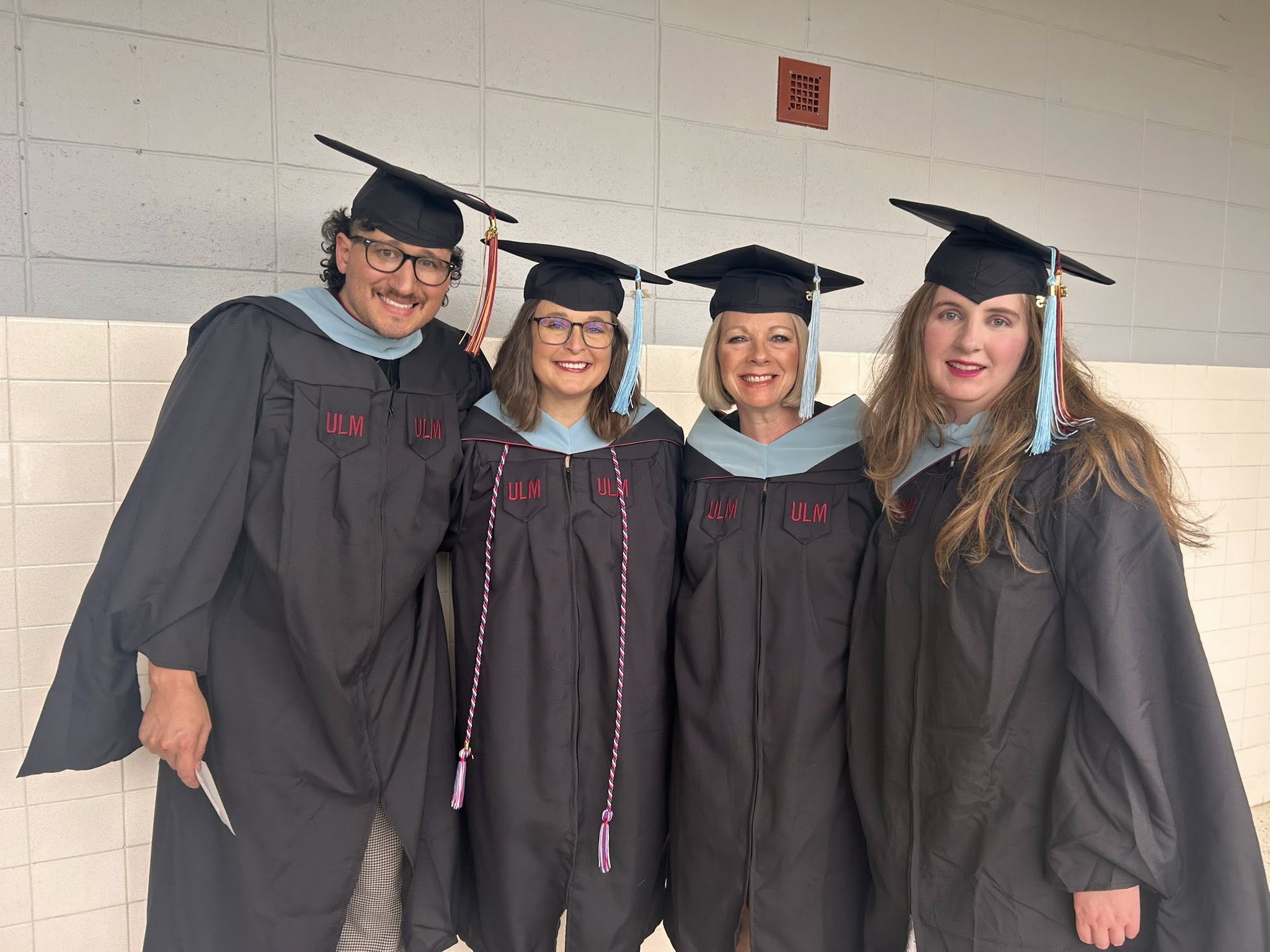 a group of graduates wearing black graduation gowns and mortarboards with "ULM" embroidered on the robe