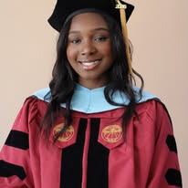 a graduate wearing a maroon doctoral gown with a light blue hood, consistent with an education doctorate