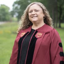 a person smiling for a portrait while wearing a maroon academic graduation gown